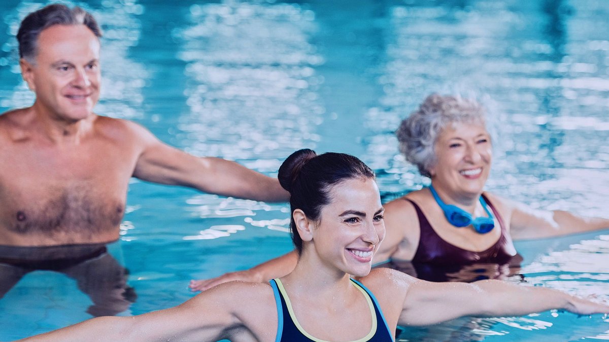 Zwei Frauen und ein Mann sind in einem Schwimmbecken und machen dort anscheinend eine Aqua-Fitness Übung.