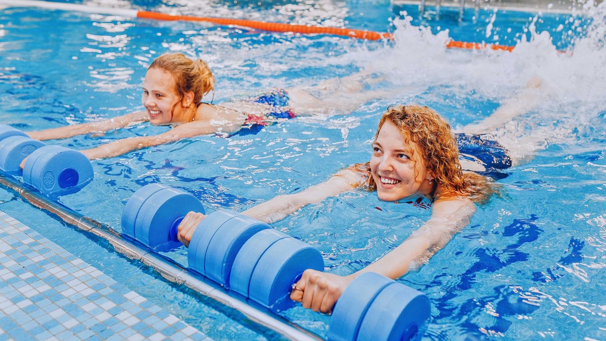 Zwei Frauen machen Wassergymnastik mit Schwimmnudeln im Schwimmbecken.