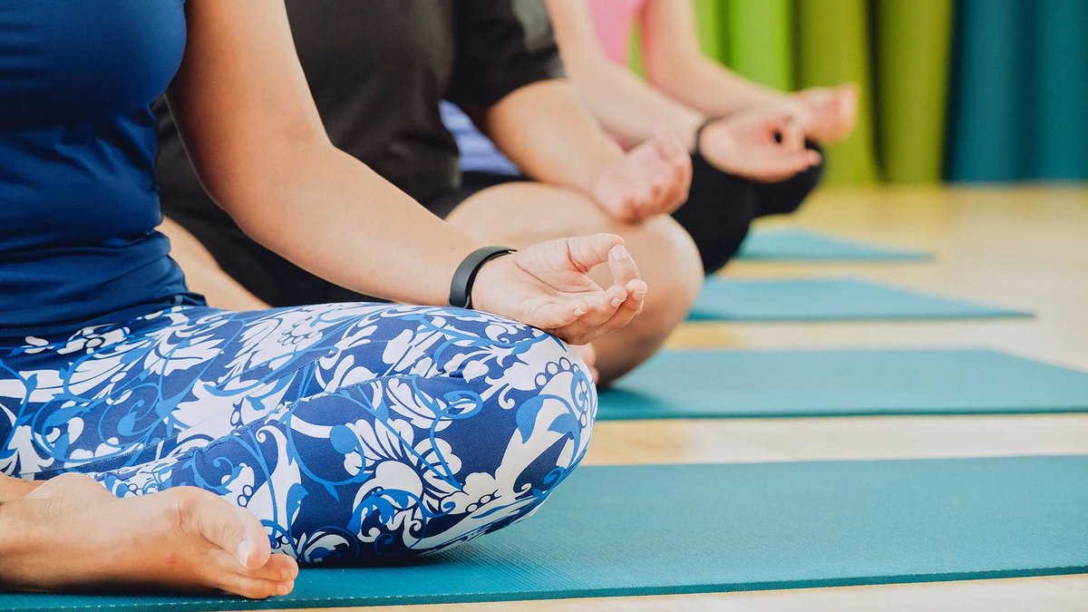 Mehrere Personen sitzen im Schneidersitz meditierend auf einer Yoga-Matte.