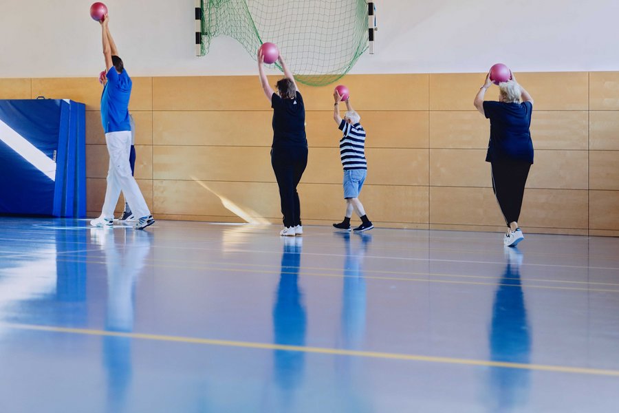 Eine Gruppe von Personen stehen in einer Sporthalle und halten alle einen Ball über ihren Kopf.